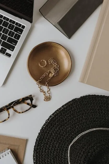 A stylish, organized desk featuring minimalist gold jewelry (necklace, bracelet, rings), a structured leather tote bag, and a pair of classic, pointed-toe pumps. The background is a clean, modern office space with natural light.