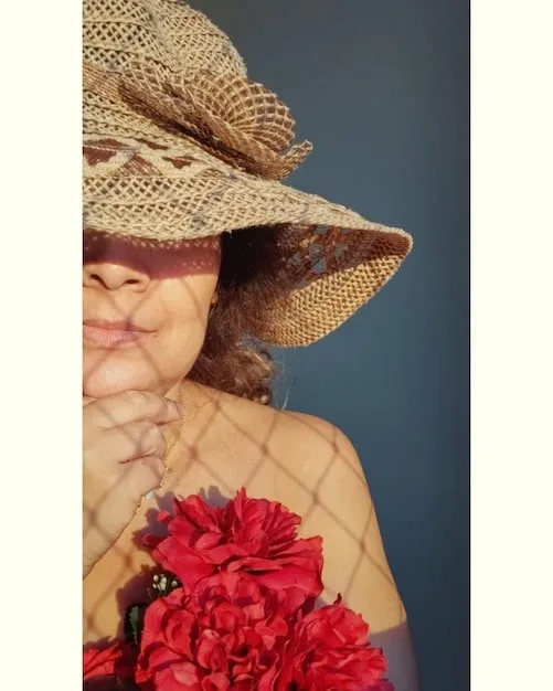 A close-up shot of a woman wearing a stylish wide-brimmed hat made of woven straw, complemented by delicate floral accents, illustrating a blend of elegance and sun protection.