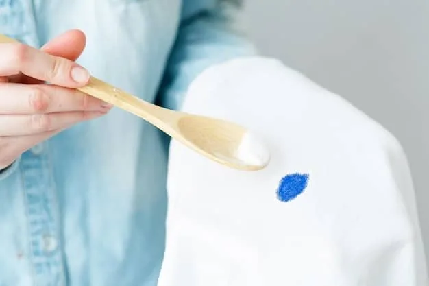 A close-up shot of a person carefully applying a stain remover to a small stain on a white cotton shirt. The focus is on the precision and gentleness of the application, highlighting the effectiveness of the product.