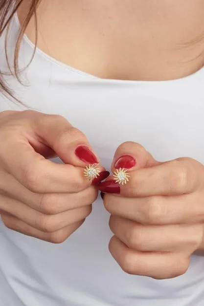 A close-up shot of a woman's hands changing earrings. One hand is removing a small stud earring, while the other is putting in a long, dangling earring with rhinestones. The background is blurred, showcasing a stylishly decorated vanity.