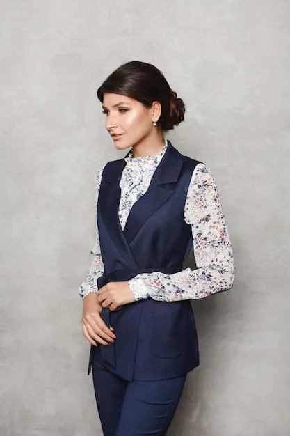 A woman in a professional office setting, wearing a layered outfit consisting of a blouse, a blazer, and a trench coat. Her accessories include a scarf and structured handbag, completing the polished look.