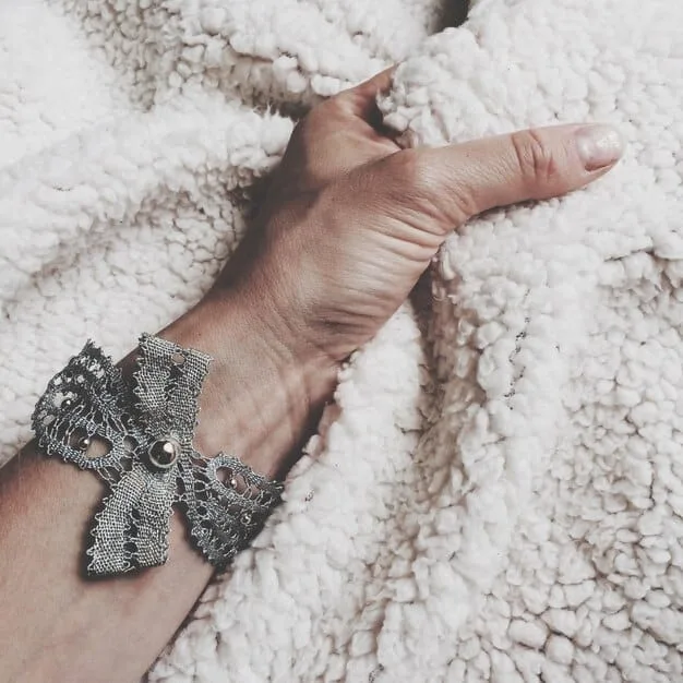 Close-up shot of a woman's hands adjusting a large, intricately designed silver cuff bracelet. The bracelet features a detailed, nature-inspired motif with leaves and vines. The background is soft and out of focus, emphasizing the craftsmanship and artistry of the statement jewelry piece.