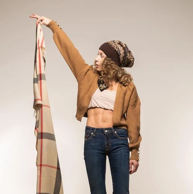 A woman styling a scarf in multiple ways, showcasing different tying techniques and how the scarf changes the overall look of a simple top.