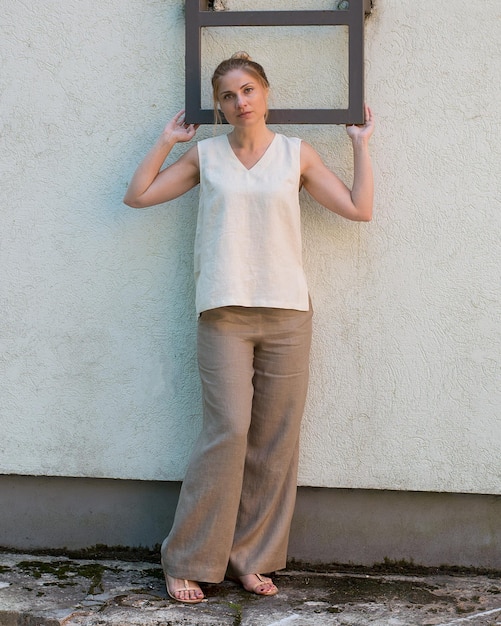 A woman wearing a neutral-toned outfit consisting of a white blouse, beige trousers, and a gray cardigan, but with a vibrant red handbag as the focal point. The background is a minimalistic studio setting.