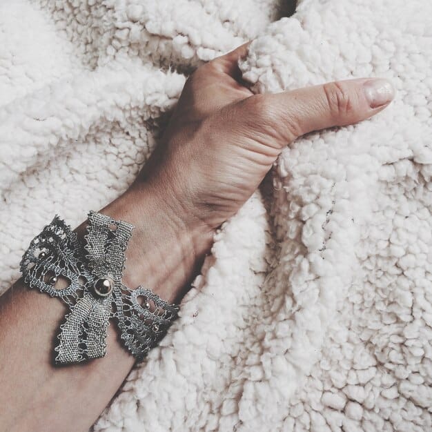 Close-up shot of a woman's hands adjusting a large, intricately designed silver cuff bracelet. The bracelet features a detailed, nature-inspired motif with leaves and vines. The background is soft and out of focus, emphasizing the craftsmanship and artistry of the statement jewelry piece.