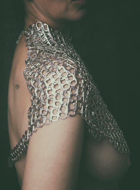 A close-up of a woman's torso showcasing a unique statement belt made of interwoven metallic chains and leather. The belt cinches a flowing, neutral-toned dress at the waist, accentuating the silhouette. The background is minimalistic to draw attention to the belt's intricate details and texture.