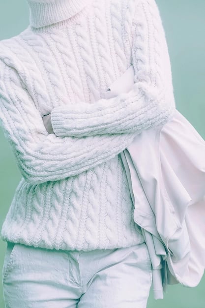 A woman wearing a monochrome minimalist outfit, featuring a chunky knit sweater paired with tailored trousers, showcasing the interplay of textures within a neutral color palette.