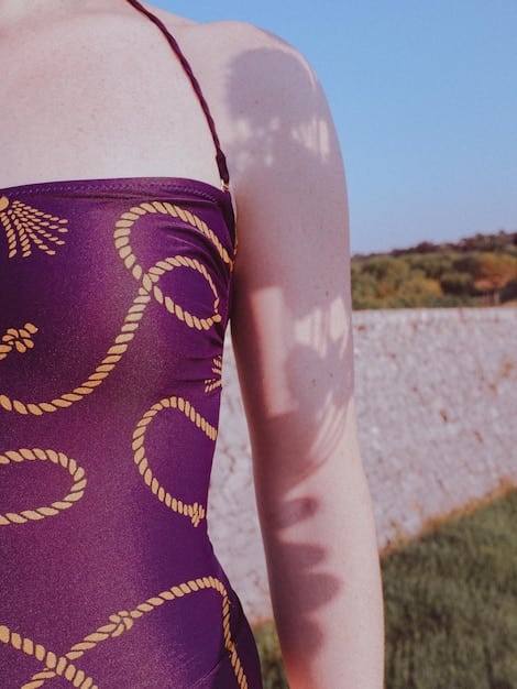 A close-up of a woman wearing a sustainable swimsuit made from recycled materials, highlighting the texture and eco-friendly aspect of the fabric. The background is a blurred image of a sunny beach.
