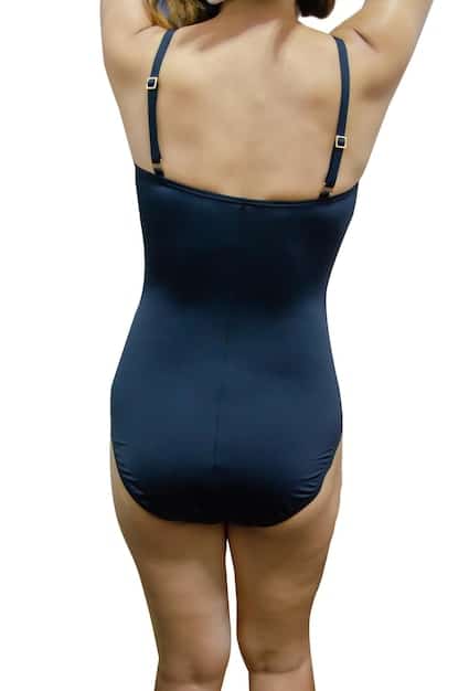 A woman wearing a one-piece swimsuit with strategic cutouts that accentuate her waistline. The swimsuit is a solid color with a minimalist design. The background is a blurred image of a luxury resort pool.