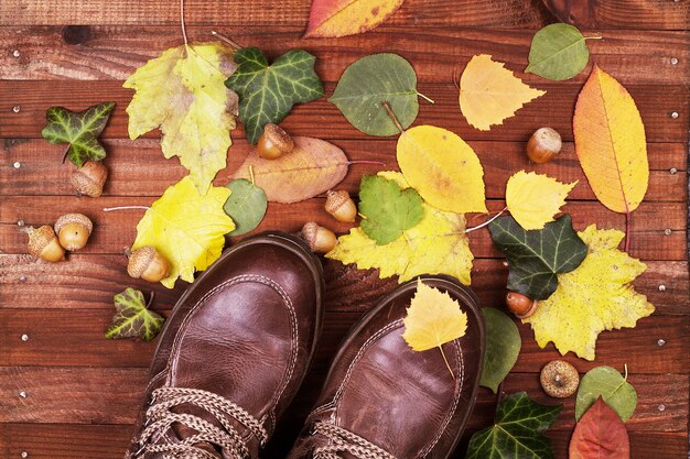 A flat lay showcasing different boot materials and colors on a wooden surface. There are swatches of leather in shades of burgundy, forest green, and dark brown, alongside suede samples in mustard yellow and deep teal. Additional elements include zippers, buckles, and textured fabrics, giving a sense of the variety and richness of the Fall 2025 boot trends.