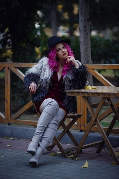 A woman wearing a long, plush faux fur coat in a vibrant color, paired with leather pants and ankle boots.