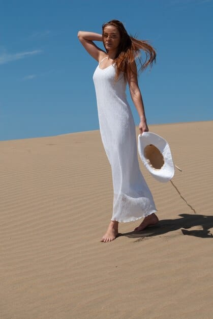 A woman walking on a beach in a wide-brimmed hat and flowing linen cover-up, carrying a beach bag, showcasing stylish sun protection.