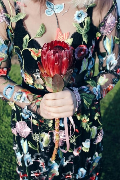 A close-up shot of a runway look featuring a model wearing a bold floral print dress. The dress has large, vibrant flowers in shades of pink, orange, and green. The background is blurred, emphasizing the intricate details of the floral design.