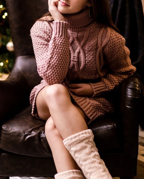A close-up of a woman wearing a burgundy leather skirt paired with a cream-colored sweater and ankle boots. The focus is on the texture and color of the leather.