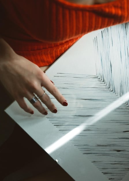A close-up shot of a designer's hands sketching a couture gown design in a sketchbook. The sketch shows intricate lace details and flowing lines, capturing the initial creative vision.