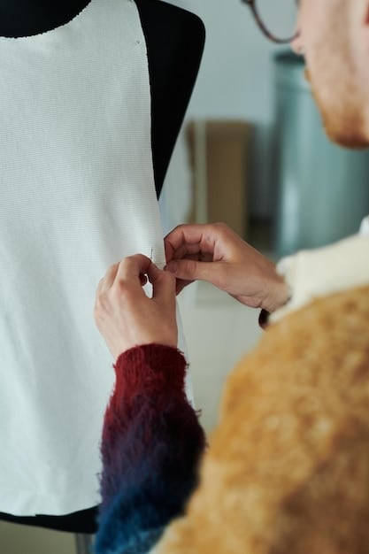 A close-up shot of a designer's hands meticulously crafting a garment. The focus is on the detail and precision of the handwork, highlighting the skill and artistry involved in the creation process. The background is a well-lit studio with various tools and materials.