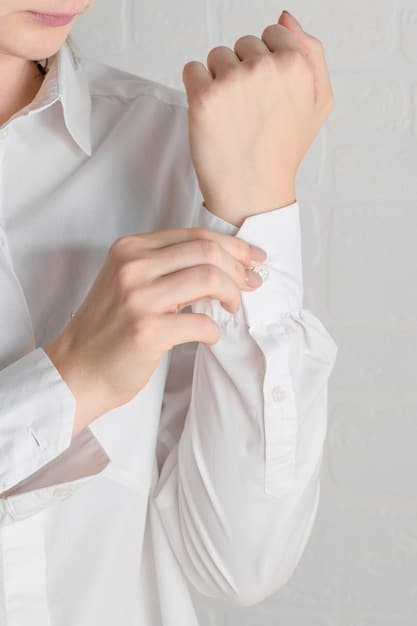 A close-up shot of a woman's hands buttoning up a crisp, white button-down shirt. The fabric is high-quality and the buttons are pearlized. The background is blurred to emphasize the texture and details of the shirt.