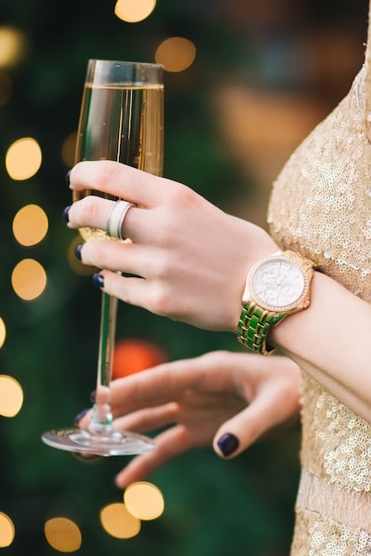 A close-up of a woman's hands elegantly accessorized with a diamond bracelet and a sophisticated watch, holding a champagne glass at a formal gala.