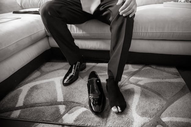 A close-up shot of a pair of well-tailored black trousers with a slight crease, paired with elegant black loafers and a simple leather belt. The background is a minimalist, modern interior.