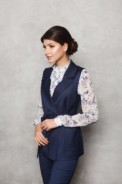 A woman in a professional office setting, wearing a layered outfit consisting of a blouse, a blazer, and a trench coat. Her accessories include a scarf and structured handbag, completing the polished look.