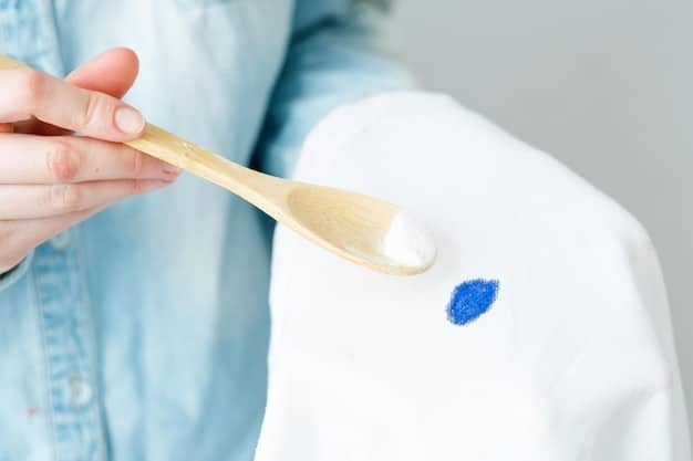A close-up shot of a person carefully applying a stain remover to a small stain on a white cotton shirt. The focus is on the precision and gentleness of the application, highlighting the effectiveness of the product.