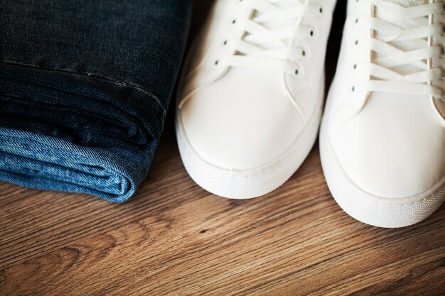 A close-up shot of dark wash jeans folded neatly, alongside a classic white t-shirt and a pair of minimalist white sneakers, emphasizing quality fabric and timeless design.