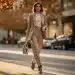 Woman in stylish layered fall outfit, wide-leg trousers, blazer, unique accessory, urban setting.